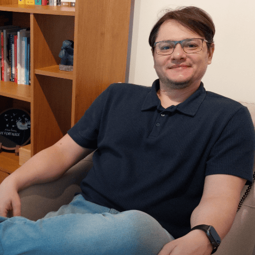Psicólogo Fabiano sentado em seu escritório com estante de livros ao fundo, representando sua sólida formação e experiência clínica